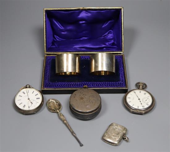 A cased pair of silver napkin rings, a silver pill box and spoon, a silver vesta case and two silver pocket watches.